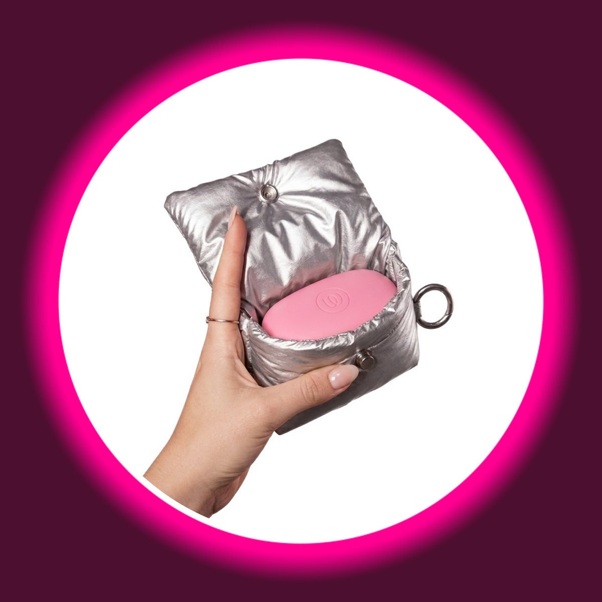 Womanizer Snap Accessory Pouch in Silber geöffnet – Hand hält gepolsterte Silber-Pouch mit rosa Womanizer Snap Ladecase darin, Schlüsselring seitlich