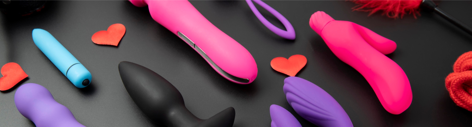diverse Sextoys in schwarz lila pink mit roten Elementen auf schwarzem Untergrund